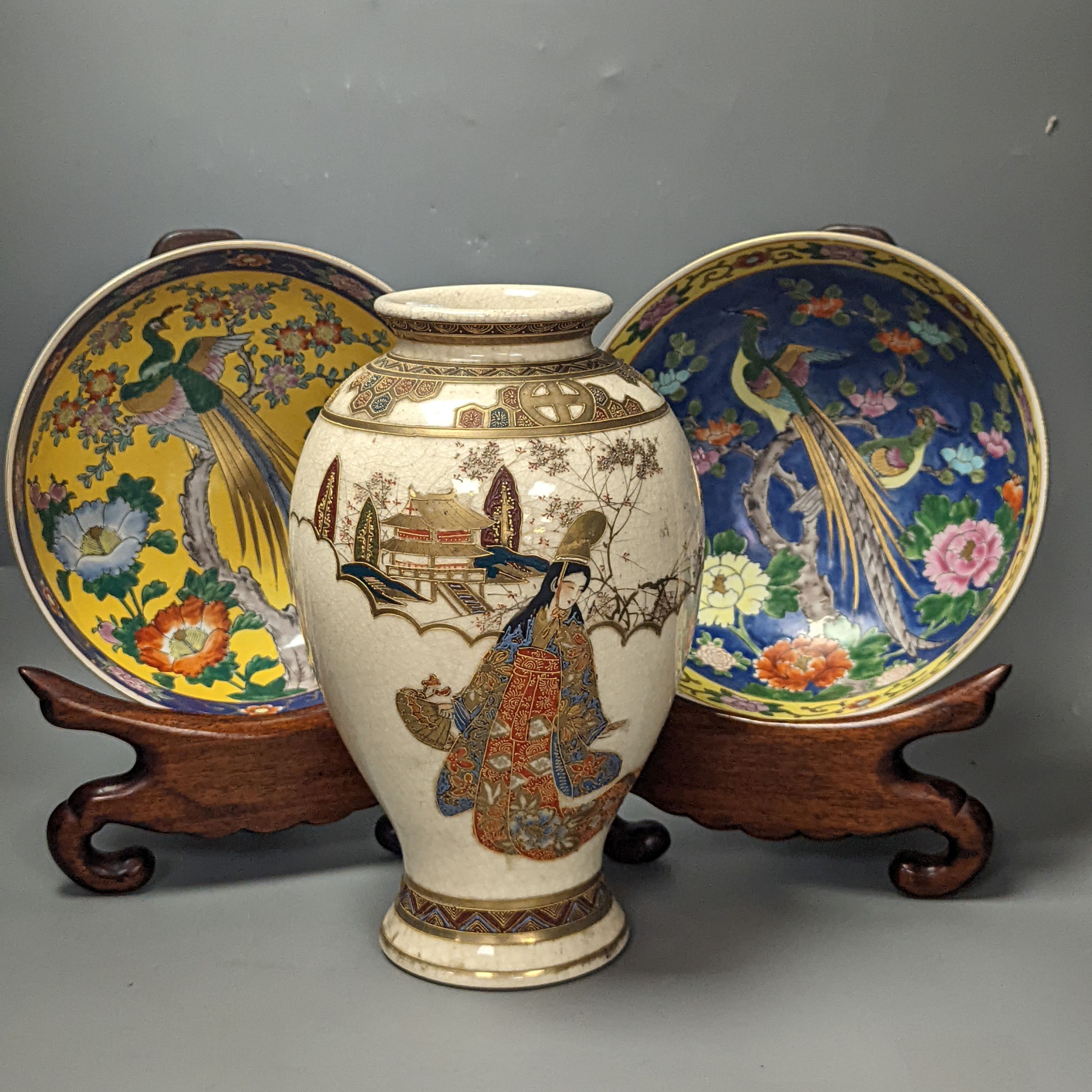 A Japanese Satsuma vase of a geisha and two Japanese yellow and a blue ground bowls each on wooden stands, Stands 32 cms high x 26cms deep.